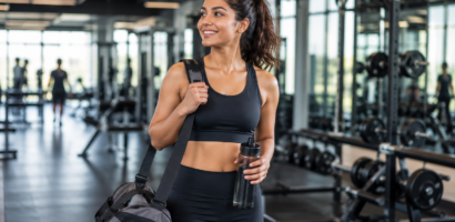 Young woman entering a modern fitness center on her first day at gym carrying a gym bag and water bottle
