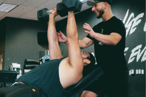 Personal trainer assisting a client with dumbbell strength training in a gym in Thane.